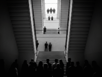 Foto em preto e branco de uma escadaria vista de baixo para cima, com silhuetas de pessoas em diferentes degraus (representa a hierarquia social)